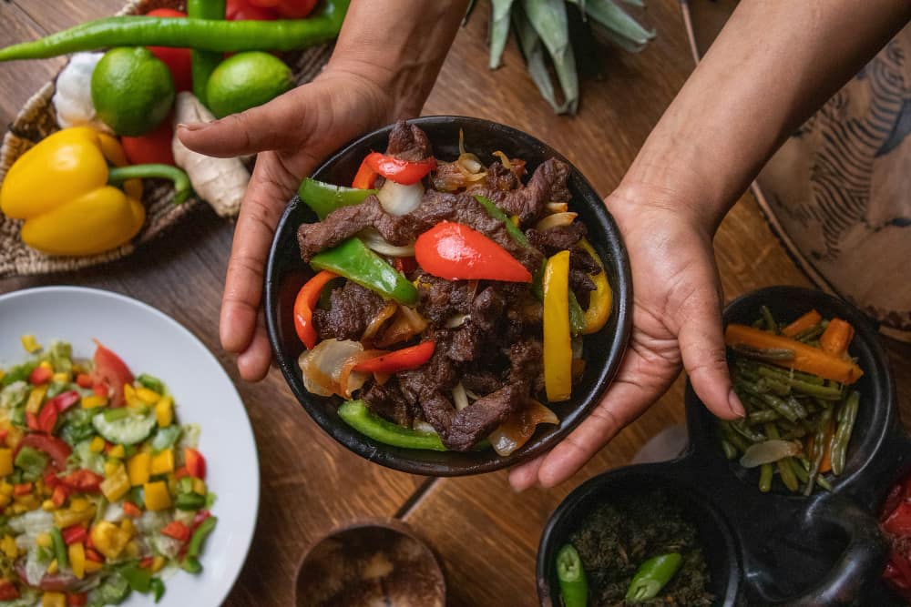 hands holding a bowl of stir-fry food.