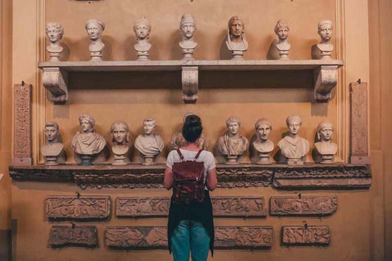 Young woman wearing a backpack and starring at busts at a museum.